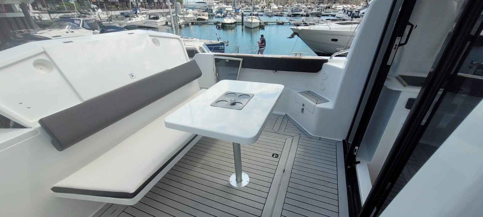 Modern boat interior with a white table, cushioned seating, and views of a marina filled with boats.